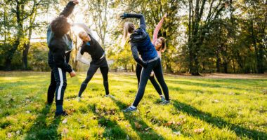 group of adults in fitness clothes stretch in a circle in a park