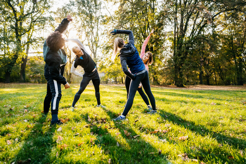 group of adults in fitness clothes stretch in a circle in a park