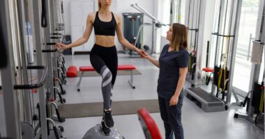 female athlete stands on a balance ball while a personal trainer assists