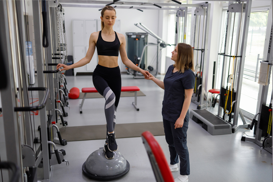 female athlete stands on a balance ball while a personal trainer assists