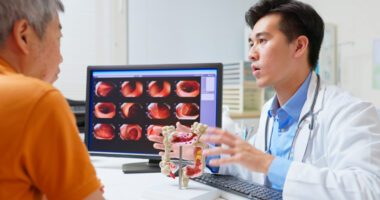 Provider speaks to patient with demonstratives of a stomach/intestine model and images of a colon on a computer screen