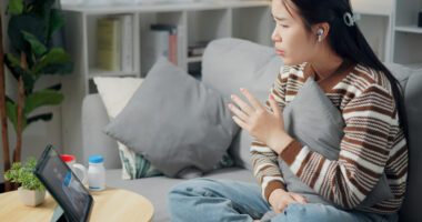 A woman participates in a virtual therapy session from home using a tablet.
