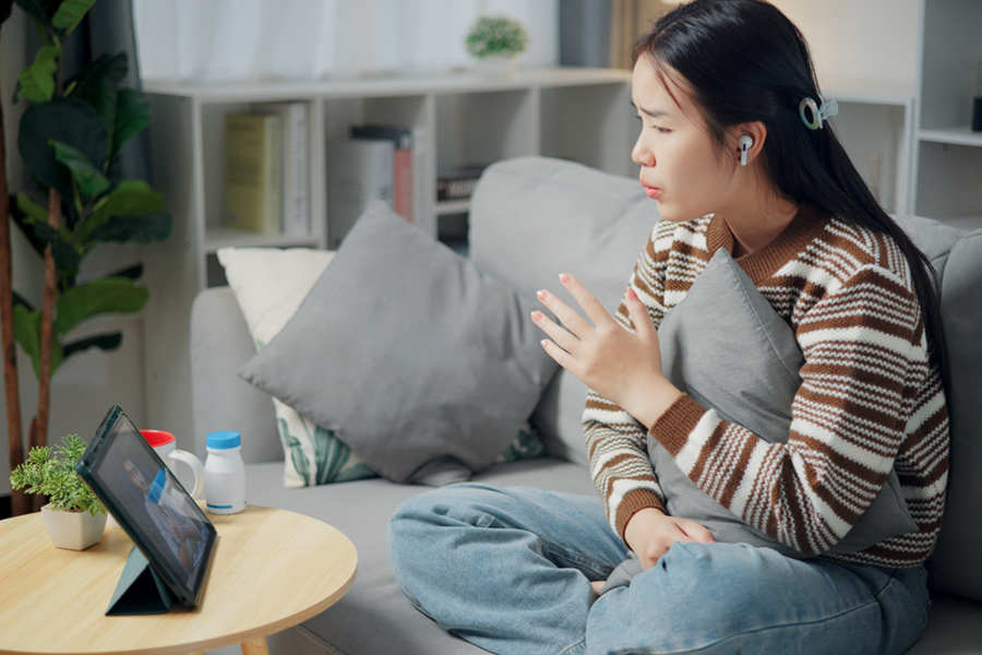 A woman participates in a virtual therapy session from home using a tablet.