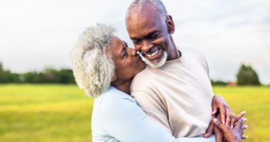 An older couple smiling and embracing outdoors.