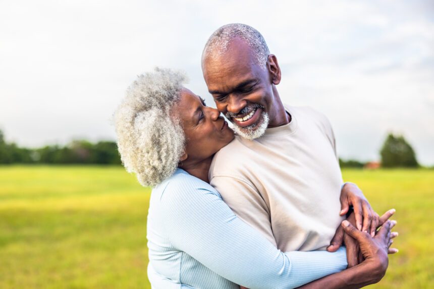 An older couple smiling and embracing outdoors.