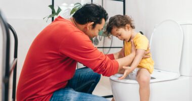 Dad hold toddler child as he sits on the toilet
