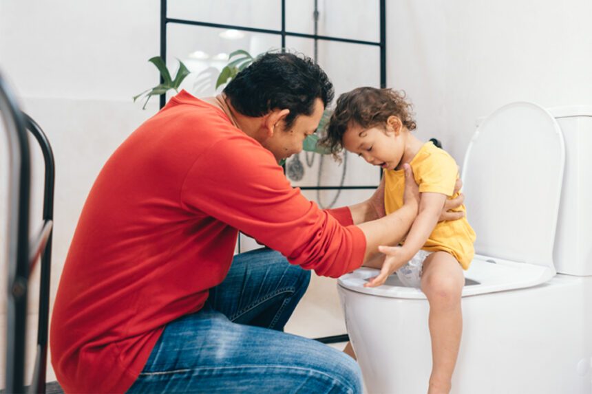 Dad hold toddler child as he sits on the toilet