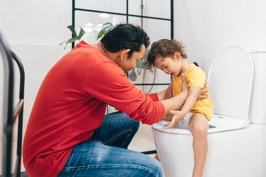 Dad hold toddler child as he sits on the toilet