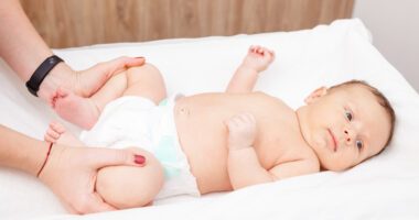 baby lays on changing table as provider gently bends the baby's leg to check their hips