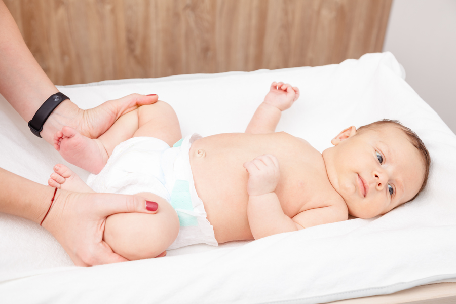 baby lays on changing table as provider gently bends the baby's leg to check their hips