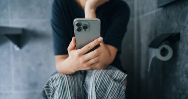 Woman looks at phone while she sits on toilet