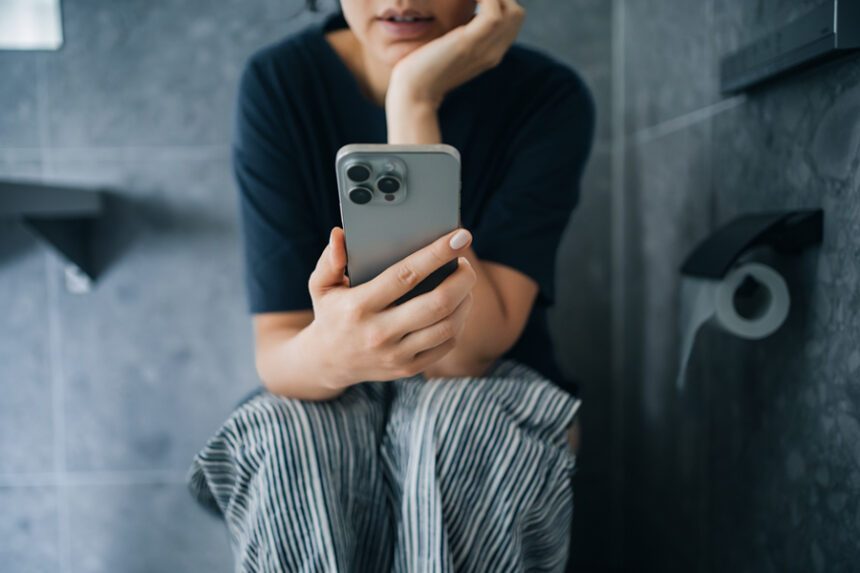Woman looks at phone while she sits on toilet