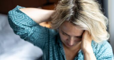 A woman looks fatigued and holds her head, appearing overwhelmed or unwell.