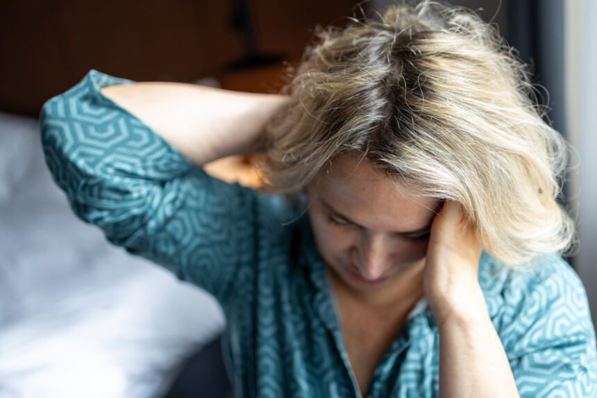 A woman looks fatigued and holds her head, appearing overwhelmed or unwell.