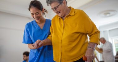 A healthcare worker assists an older woman with walking during a rehabilitation session.