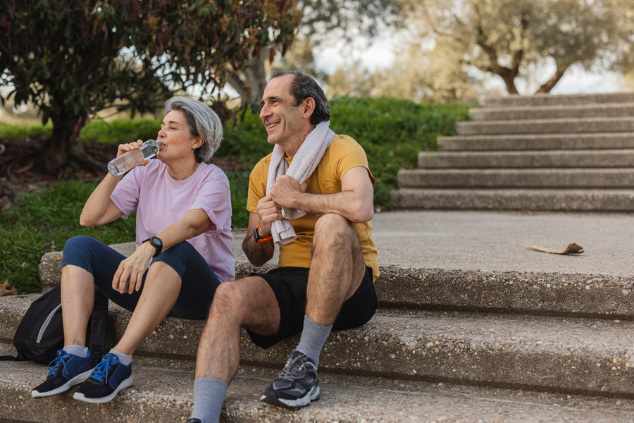 Two people sitting on a staircase drinking water after exercising.