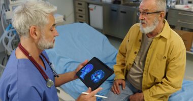 provider holds tablet with image of brain scan on screen; discusses with patient sitting on exam table
