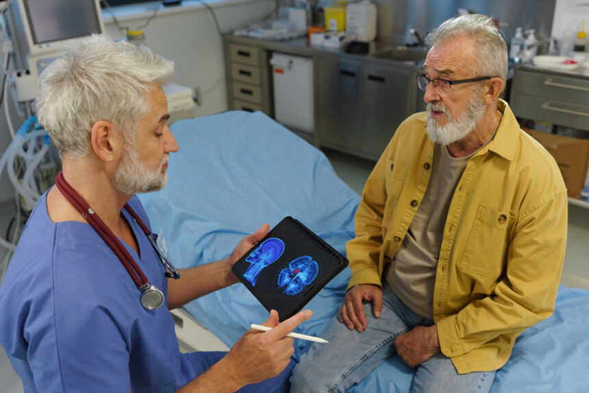 provider holds tablet with image of brain scan on screen; discusses with patient sitting on exam table