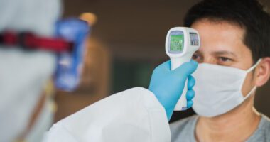 patient wearing face mask has temperature checked by a provider wearing medical gloves