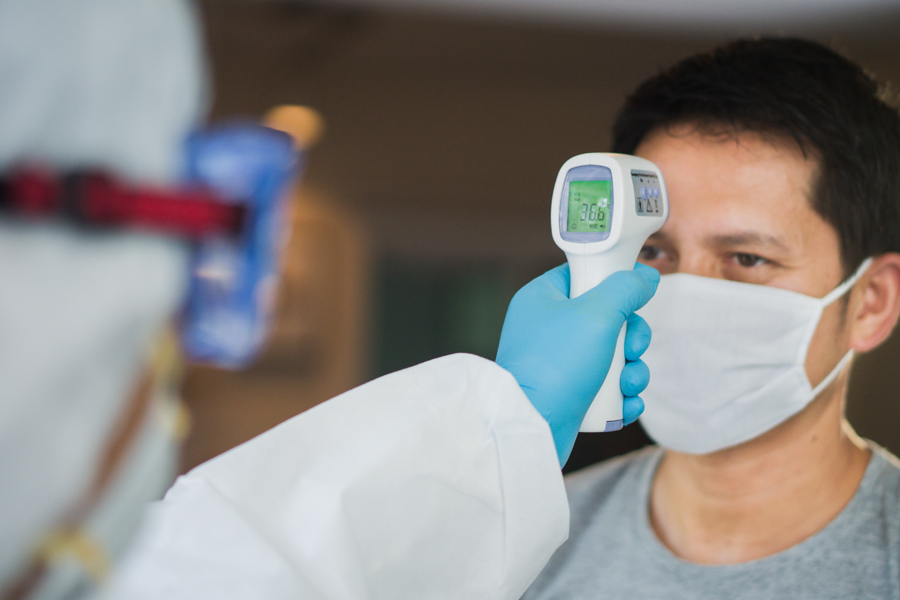 patient wearing face mask has temperature checked by a provider wearing medical gloves