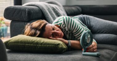 Middle-aged woman lies on couch with fan aimed at her face
