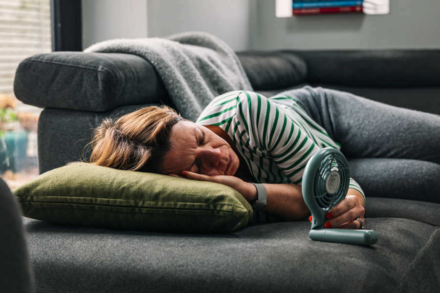 Middle-aged woman lies on couch with fan aimed at her face