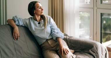 Woman sits on a couch and looks pensive.