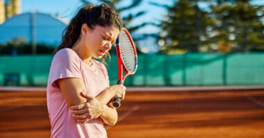female tennis player grabs elbow in pain while holding tennis racket in other hand