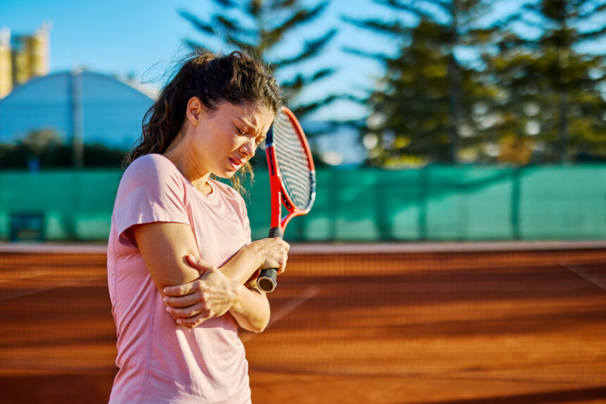female tennis player grabs elbow in pain while holding tennis racket in other hand