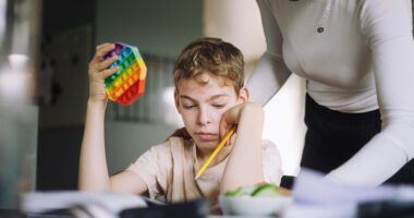 A child works on schoolwork with support from an adult, demonstrating focus and guidance during a learning activity.
