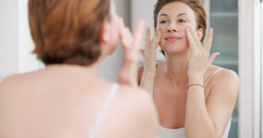A woman applies a skincare product while looking at herself in the mirror.
