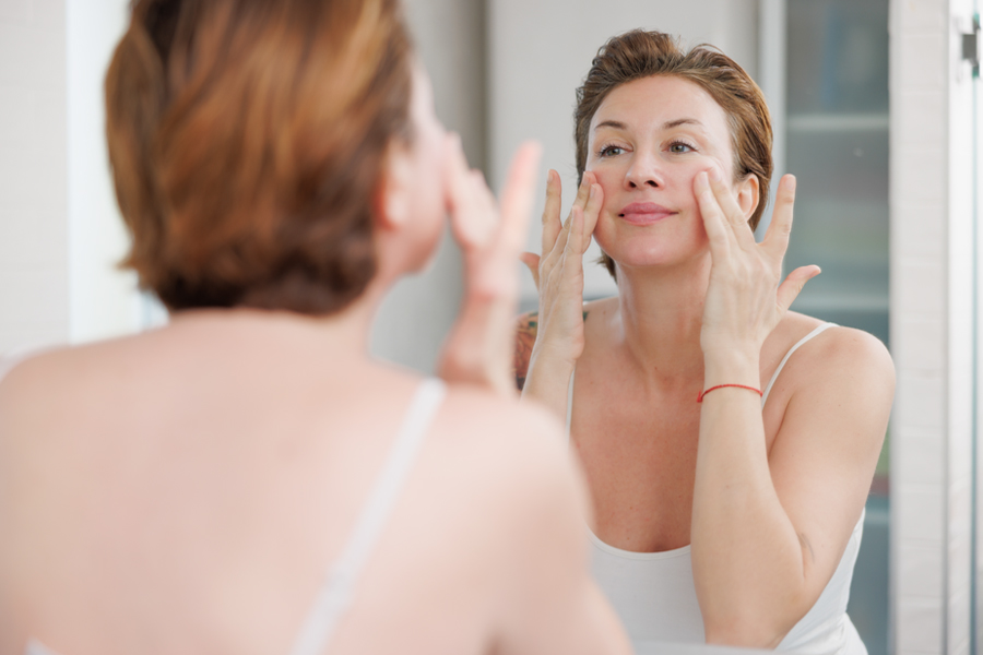 A woman applies a skincare product while looking at herself in the mirror.