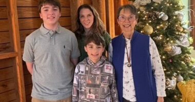 Ann Herndon poses with her two grandsons and a family member in front of a decorated Christmas tree, celebrating time together during the holidays.