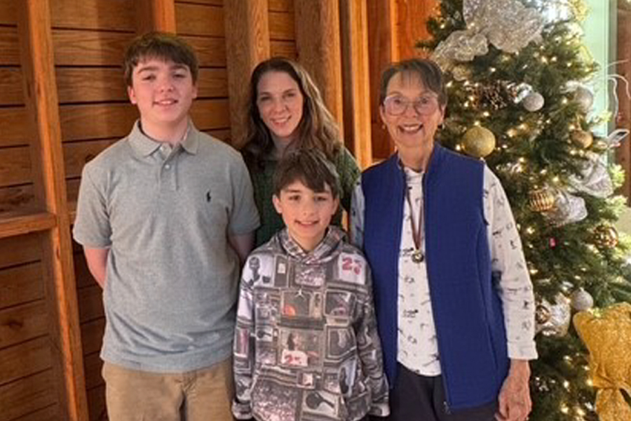 Ann Herndon poses with her two grandsons and a family member in front of a decorated Christmas tree, celebrating time together during the holidays.