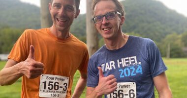 Two runners smile and give a thumbs-up after a race in the mountains.