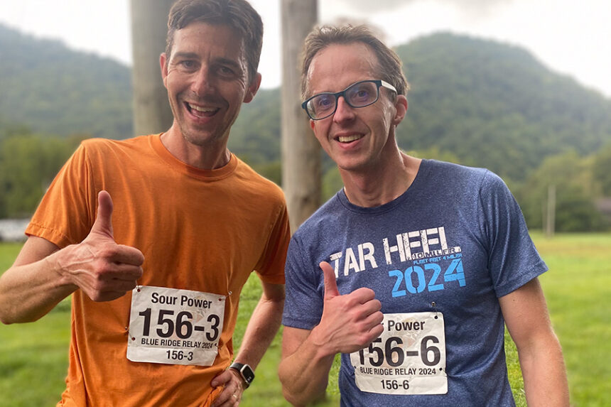 Two runners smile and give a thumbs-up after a race in the mountains.