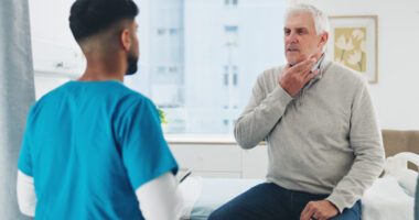 An older adult receives a throat evaluation from a healthcare provider.