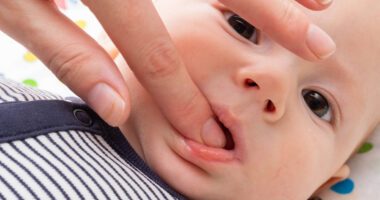 An adult gently checks a baby’s gums for signs of teething.