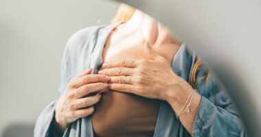Woman touching her chest while wearing a robe.”