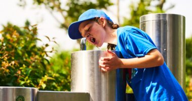 boy drinks from water fountain on a sunny day