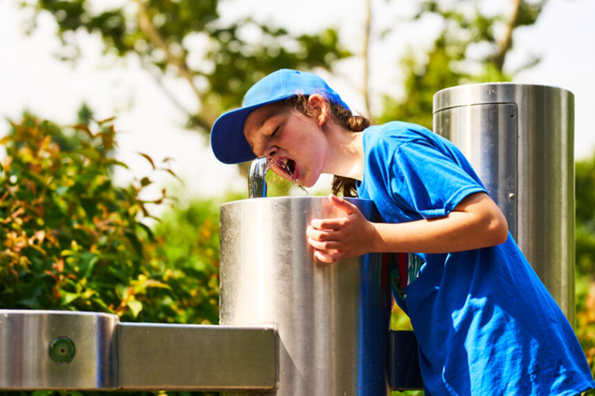 boy drinks from water fountain on a sunny day