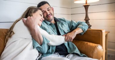 A couple sits closely together on a couch, comforting each other.