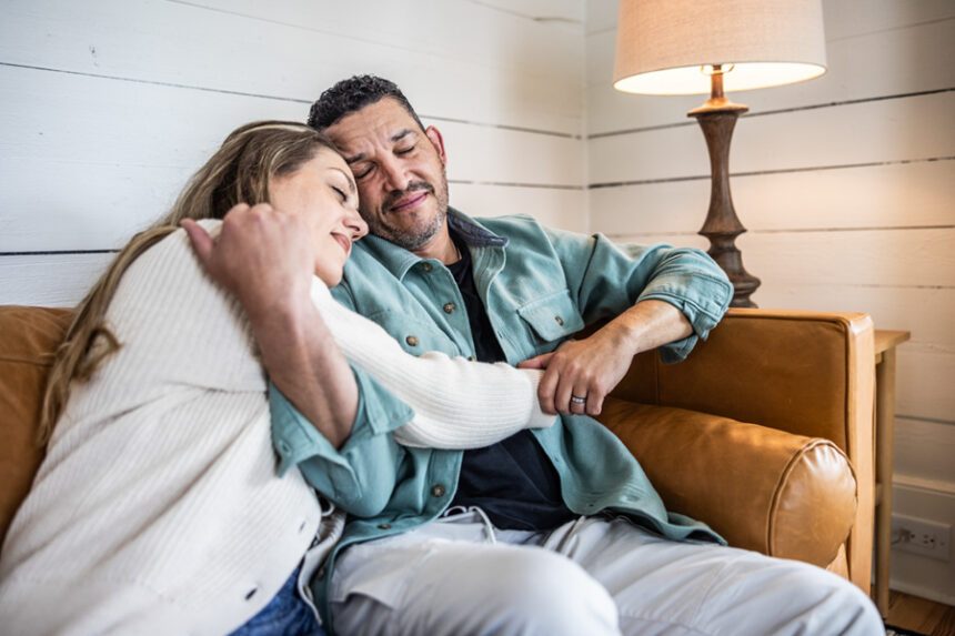 A couple sits closely together on a couch, comforting each other.