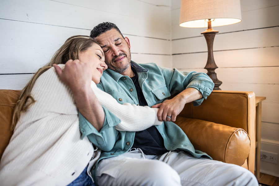 A couple sits closely together on a couch, comforting each other.