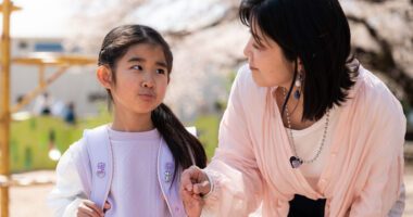 A mother talks with her young daughter outside as the child wears a backpack for school.