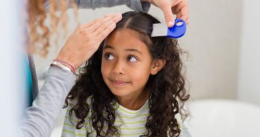A woman carefully checks a young girl’s hair for head lice using a lice comb.