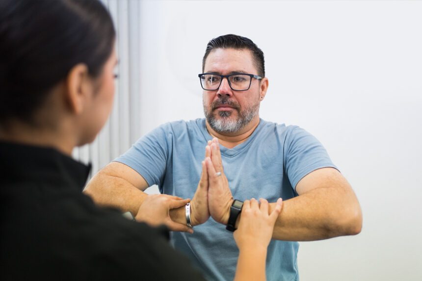 A man performs a hand coordination exercise with assistance from a healthcare professional.