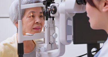 A patient receives an eye exam using specialized equipment while a healthcare professional evaluates her eyes.