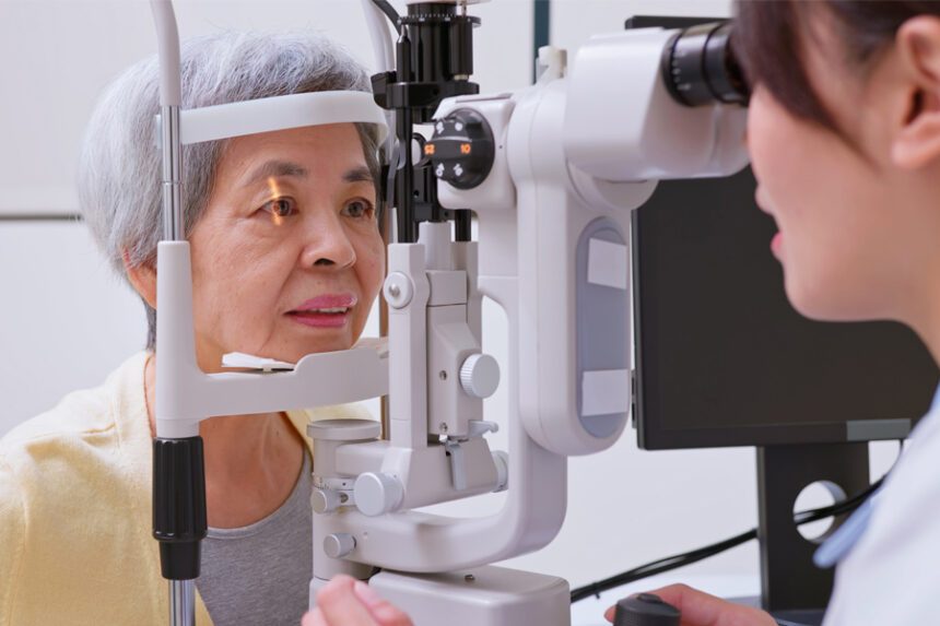 A patient receives an eye exam using specialized equipment while a healthcare professional evaluates her eyes.