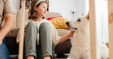girl pets her dog on a living room floor